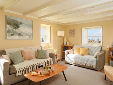 A living room with two sofas and a wooden coffee table with food and wine at Faraway Cottage in St Levan near Porthgwarra