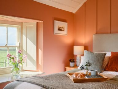 A bedroom with a bed tray holding croissants cup and a book near a window with flowers at Faraway Cottage in St Levan near Porthgwarra
