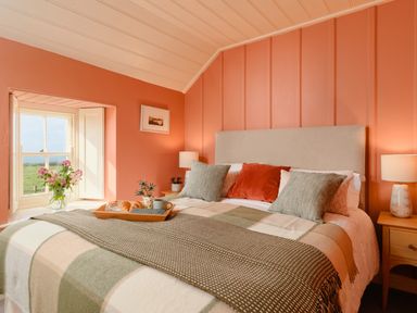 A bedroom with a double bed with cushions a wooden tray with breakfast and a window with flowers at Faraway Cottage in St Levan near Porthgwarra