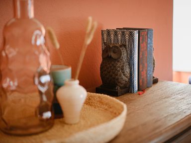 A wooden surface with owl bookends holding three books and a woven tray with vases at Faraway Cottage in St Levan near Porthgwarra