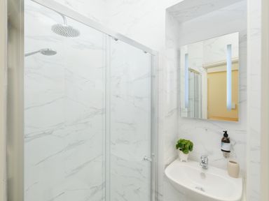 A bathroom with a glass shower enclosure a sink with a plant soap dispenser and a mirror at Faraway Cottage in St Levan near Porthgwarra