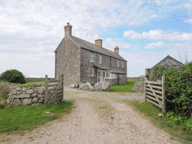 A stone house with chimneys and a gravel driveway with open wooden gates at Three Chimneys St Levan near Porthgwarra