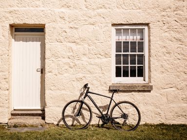 A black bicycle leaning against a stone wall next to a closed white door and a window with white frames