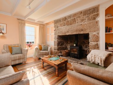 A living room with armchairs a wooden coffee table a stone fireplace and a window at Three Chimneys in St Levan near Porthgwarra
