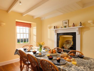A dining room with a table set for breakfast and a fireplace at Three Chimneys in St Levan near Porthgwarra