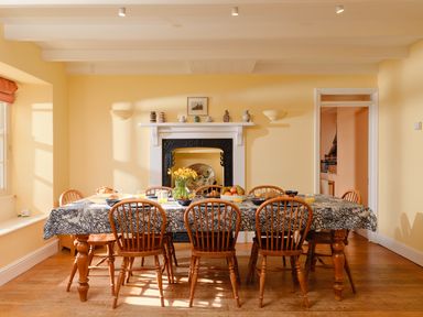 A dining room with a table and wooden chairs near a fireplace at Three Chimneys in St Levan near Porthgwarra