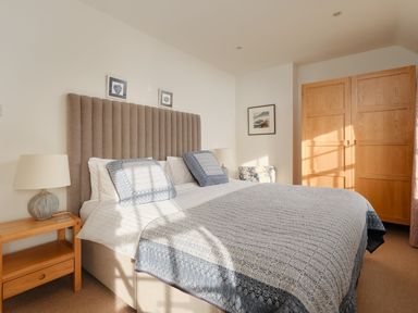 A bedroom with a double bed bedside tables lamps a wooden wardrobe and framed pictures at Three Chimneys in St Levan near Porthgwarra