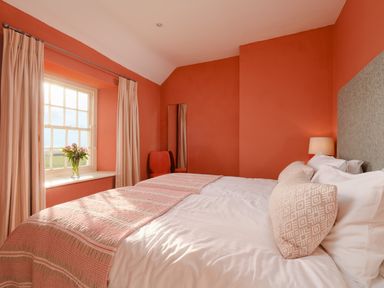A bedroom with a double bed bedside lamp chair window with curtains and flowers on the sill at Three Chimneys in St Levan near Porthgwarra