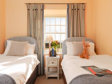 A bedroom with two single beds a bedside table a lamp and a window at Three Chimneys St Levan near Porthgwarra