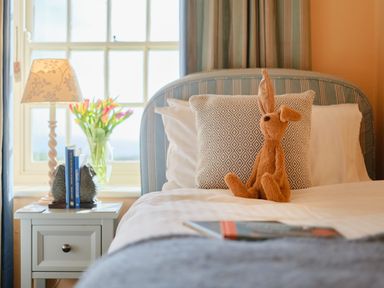 A bedroom with a bed a bedside table with a lamp and flowers at Three Chimneys in St Levan near Porthgwarra