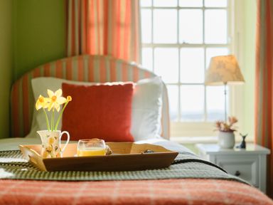 A bed with a wooden tray holding a jug with yellow flowers and a glass of orange juice at Three Chimneys in St Levan near Porthgwarra