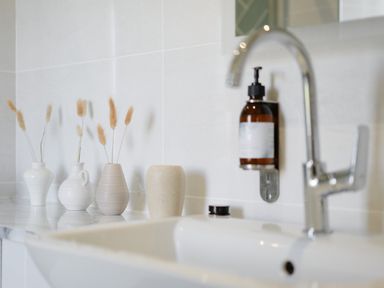 A bathroom sink with a chrome faucet soap dispenser and four small vases with dried flowers at Three Chimneys in St Levan near Porthgwarra