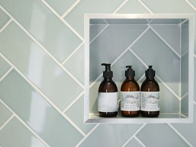 A shower niche with three pump bottles of hand and body wash on blue tiled wall at Three Chimneys in St Levan near Porthgwarra