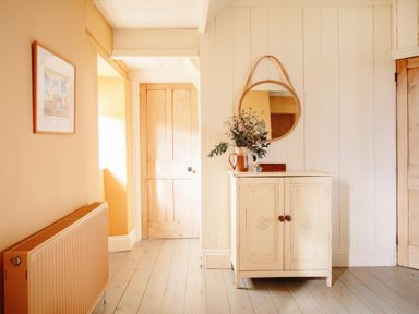 A hallway with a small cabinet a round mirror and a wooden door at Higher Roskestal in St Levan near Porthgwarra