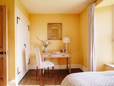 A bedroom with a wooden desk and chair a vase with flowers a lamp and a mirror at Higher Roskestal St Levan near Porthgwarra