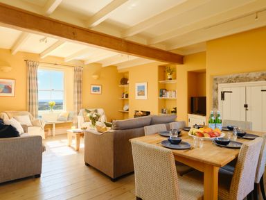 A living room with sofas a coffee table a dining table set with plates and glasses and a window with curtains at Higher Roskestal St Levan near Porthgwarra