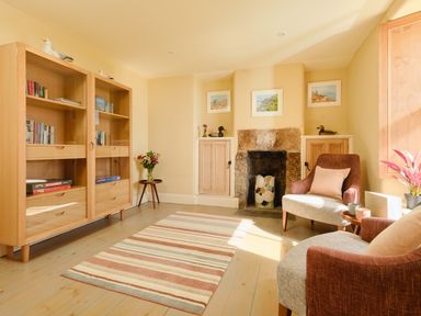 A living room with bookshelves a fireplace two armchairs and a striped rug at Higher Roskestal St Levan near Porthgwarra