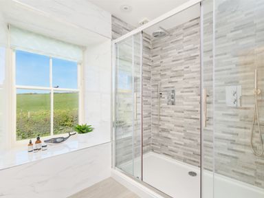 A bathroom with a glass shower enclosure a tiled shower wall and a window with items on the sill at Higher Roskestal St Levan near Porthgwarra