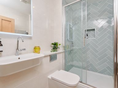 A bathroom with a wall-mounted sink a toilet and a corner shower with glass doors at Higher Roskestal in St Levan near Porthgwarra