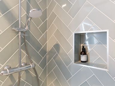 A shower area with chrome showerhead and faucet and a built-in tiled niche with a bottle at Higher Roskestal St Levan near Porthgwarra