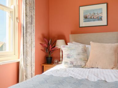 A bedroom with a bed pillows bedside table lamp plant and a window at Higher Roskestal in St Levan near Porthgwarra