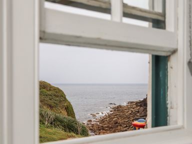 A view of a rocky coastline and ocean seen through a window at Corner Cottage in Porthgwarra