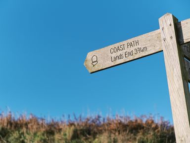 A wooden signpost indicating coast path to Lands End 3 3 quarter miles with grass and blue sky