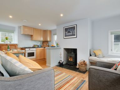 A living room with a fireplace a kitchen with wooden cabinets and a dining table at Corner Cottage in Porthgwarra
