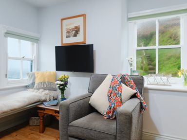 A sitting area with a gray armchair and a daybed near two windows at Corner Cottage in Porthgwarra