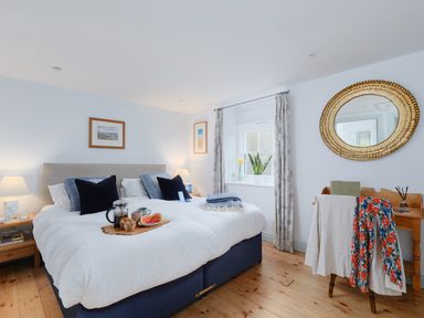 A bedroom with a double bed bedside tables window and a round mirror at Corner Cottage in Porthgwarra