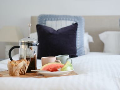 A bed with a tray holding a French press coffee maker, two cups, muffins, and slices of watermelon at Corner Cottage in Porthgwarra