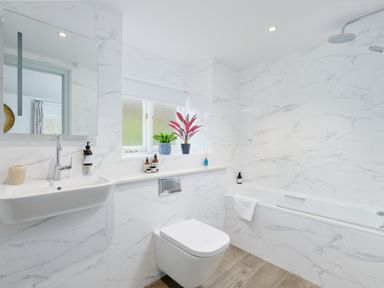 A bathroom with a wall-mounted sink bathtub toilet and plants on the windowsill at Corner Cottage in Porthgwarra