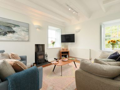 A living room with sofas cushions a coffee table a television and flowers at Cove Cottage in Porthgwarra