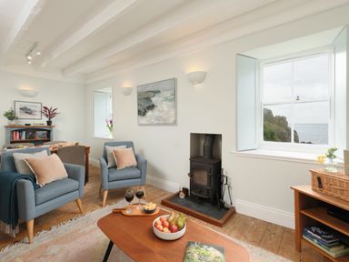A living room with two blue armchairs a wood stove and a coffee table with fruit and wine at Cove Cottage in Porthgwarra