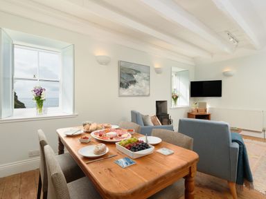A dining table with food and chairs in a living room with windows showing the sea at Cove Cottage in Porthgwarra