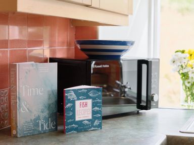 A kitchen counter with two cookbooks a microwave and a striped bowl at Cove Cottage in Porthgwarra