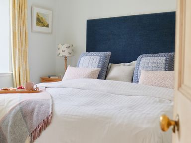 A bedroom with a bed with blue and pink pillows and a tray with a cup and snacks at Cove Cottage in Porthgwarra
