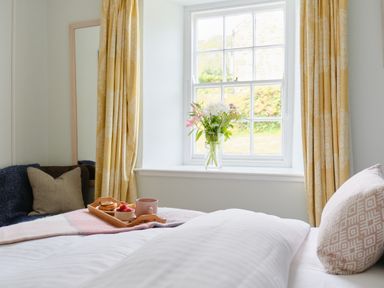 A bedroom with a bed a window with flowers and yellow curtains at Cove Cottage in Porthgwarra