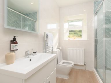 A bathroom with a sink, toilet, towel rack, shower enclosure, and window at Cove Cottage in Porthgwarra