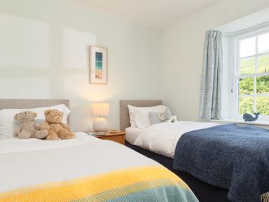 A bedroom with two single beds two teddy bears on one bed and a window with blue curtains at Cove Cottage in Porthgwarra