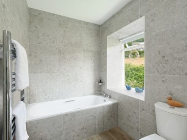 A bathroom with a bathtub a window with decorations a toilet and towels on a rack at Cove Cottage in Porthgwarra