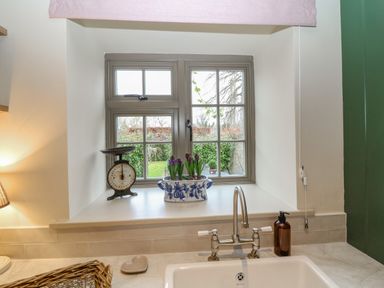 A kitchen window with a vintage scale and blue and white flower pot with flowers above a sink at Omas Cottage in Moreton-In-Marsh