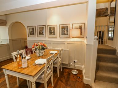 A dining room with wooden table set for four with wine bottles and flowers on the table at Oma's Cottage in Moreton-In-Marsh