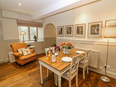 A dining area with a wooden table set for four and an armchair next to a window at Omas Cottage in Moreton In Marsh