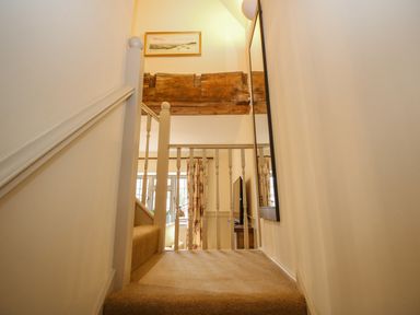 A carpeted staircase landing with white railing a wooden beam a framed painting and a mirror at Omas Cottage in Moreton In Marsh