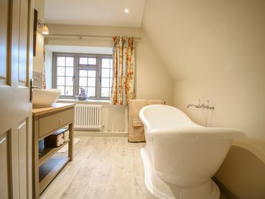 A bathroom with a freestanding bathtub a sink with cabinet and window with floral curtains at Omas Cottage in Moreton In Marsh