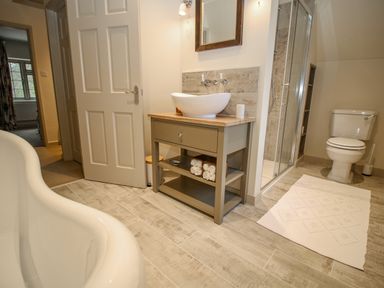 A bathroom with a bathtub a vanity with a vessel sink a mirror a shower enclosure and a toilet at Omas Cottage in Moreton-In-Marsh