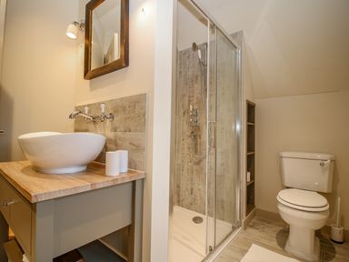 A bathroom with a sink on a wooden counter a mirror a shower with glass doors and a toilet at Omas Cottage in Moreton-In-Marsh