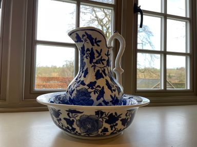 A blue and white ceramic pitcher and basin set on a windowsill with a window and outdoor view in the background at Omas Cottage in Moreton-In-Marsh