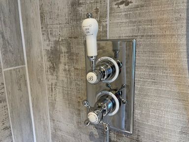 A close-up of a chrome shower control panel with on off and hot cold handles at Omas Cottage in Moreton-In-Marsh